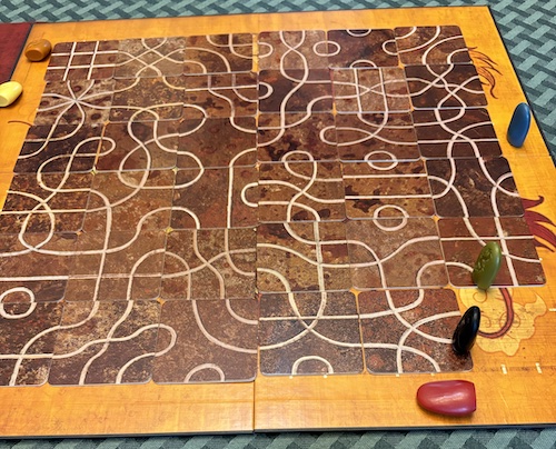 photo of game board with tiles of twisty paths, and one square left uncovered with two pieces still on the board.